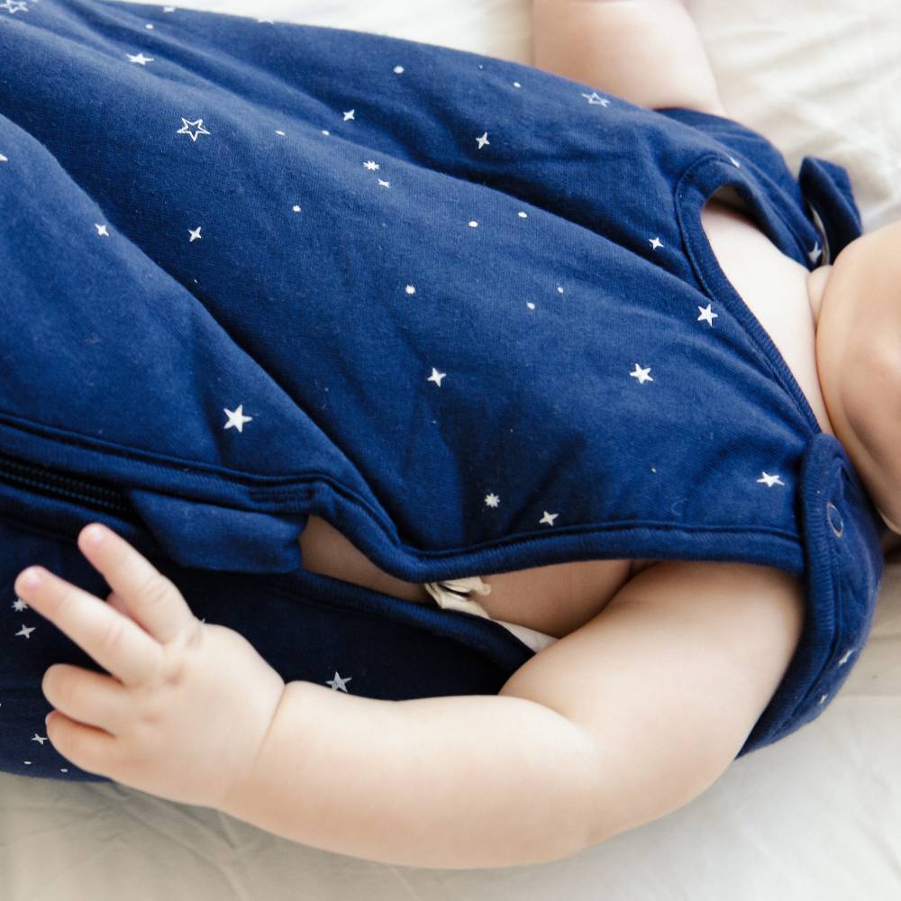 Baby wearing a navy blue duvet woolbabe with shoulder snaps with star patterns on a light background