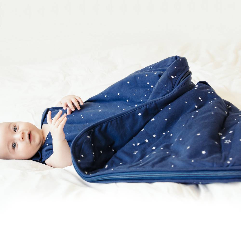 Baby lying on a white sleeping bag with a blue star-patterned swaddle.