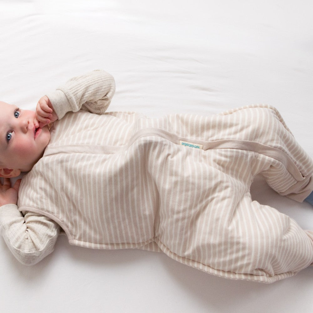 Baby lying on a white surface wearing a beige striped onesie.