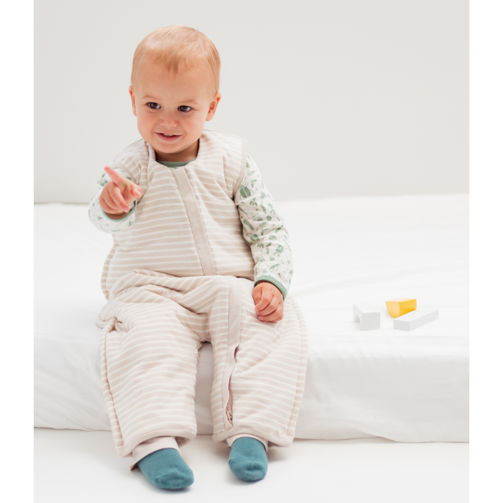 Baby wearing a quilted outfit sitting on a white couch.