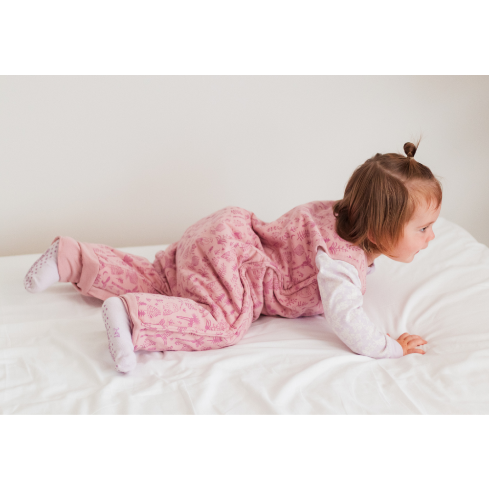 Child in pink merino sleepsuit lying on a white bed