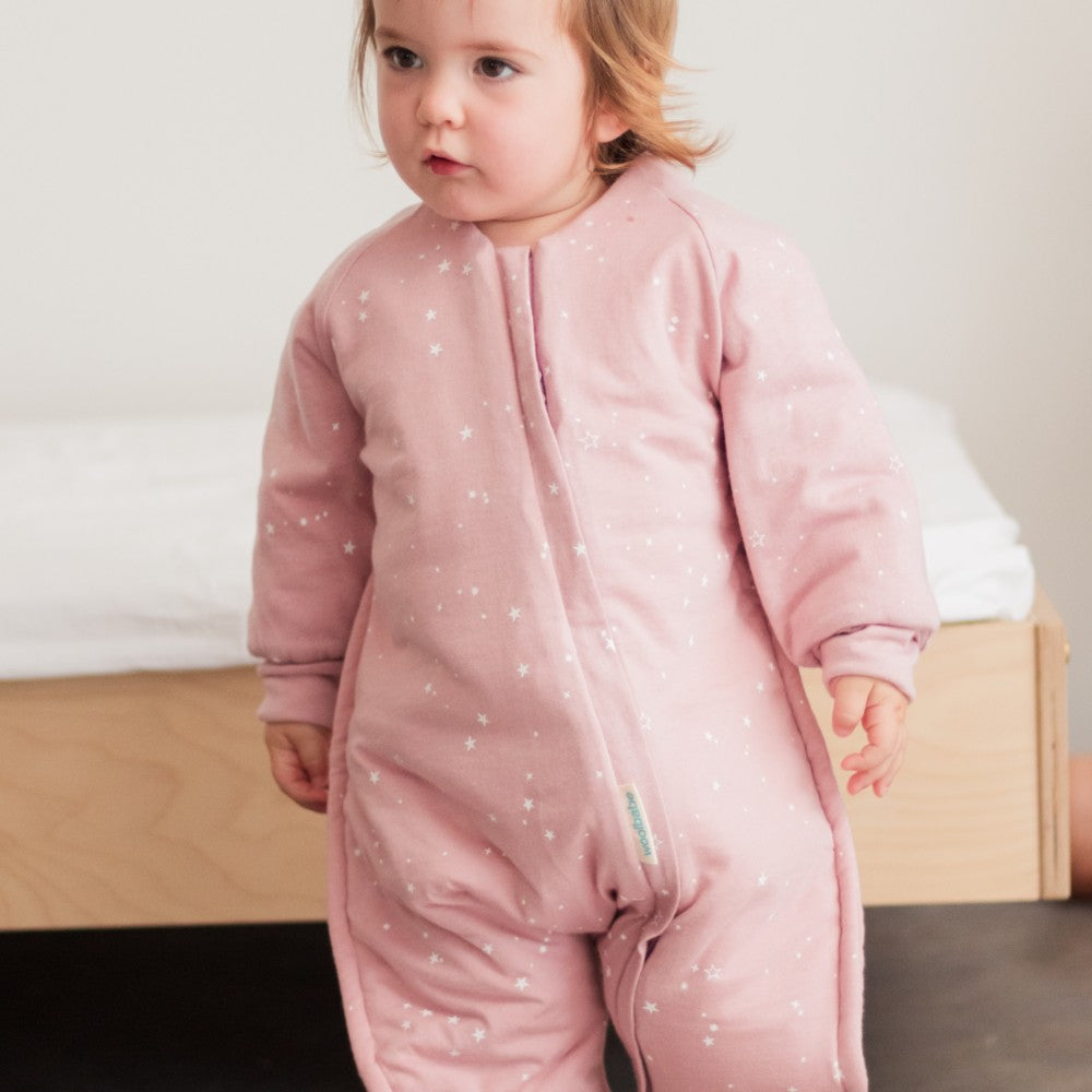 Child wearing a pink onesie with star pattern standing in a room.