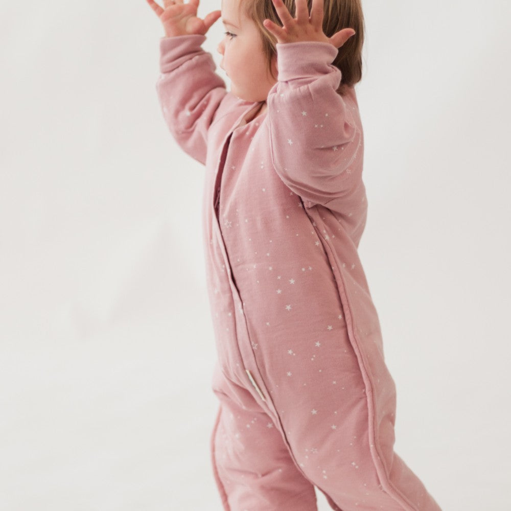 Child wearing a pink onesie with white patterns on a light background