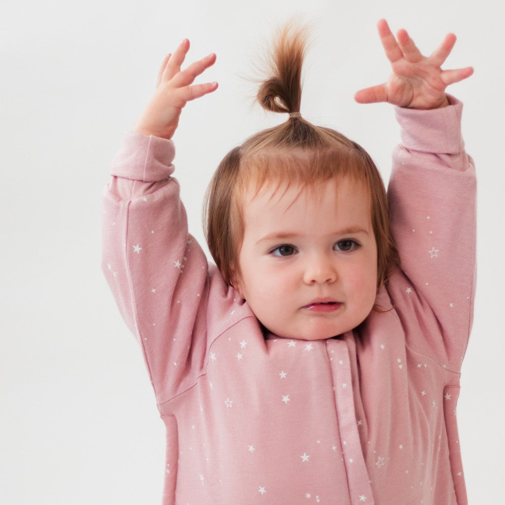 Child wearing a pink winter sleep onesie with star patterns against a white background