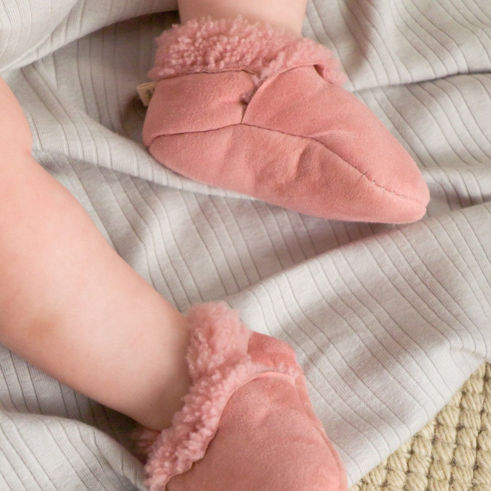 Baby's feet wearing pink fuzzy socks on a striped blanket