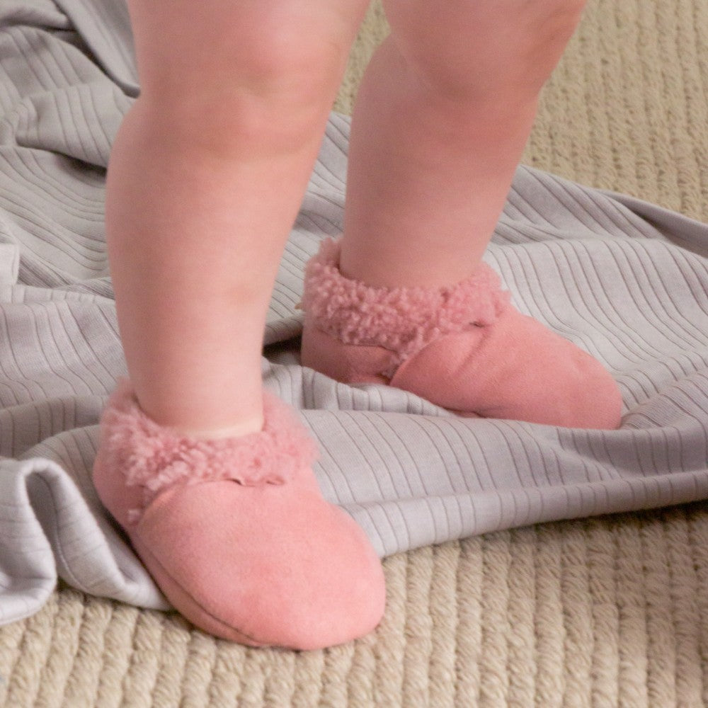 Baby feet wearing pink fuzzy socks on a textured surface