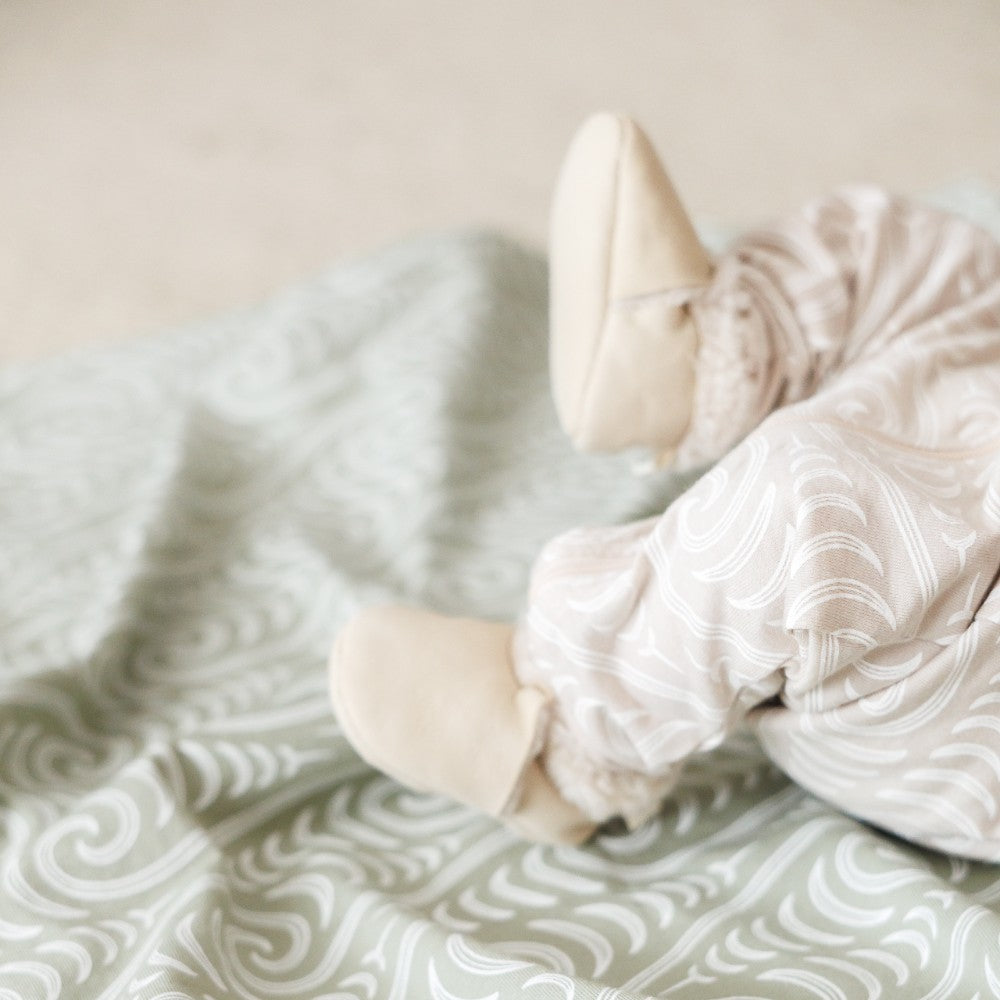 Baby in patterned outfit lying on a textured blanket with a soft focus background