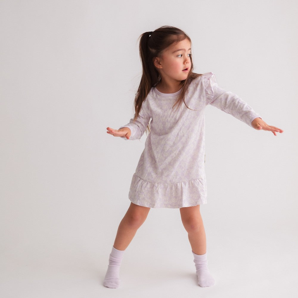 Young girl wearing a light mauve floral merino dress on a plain background