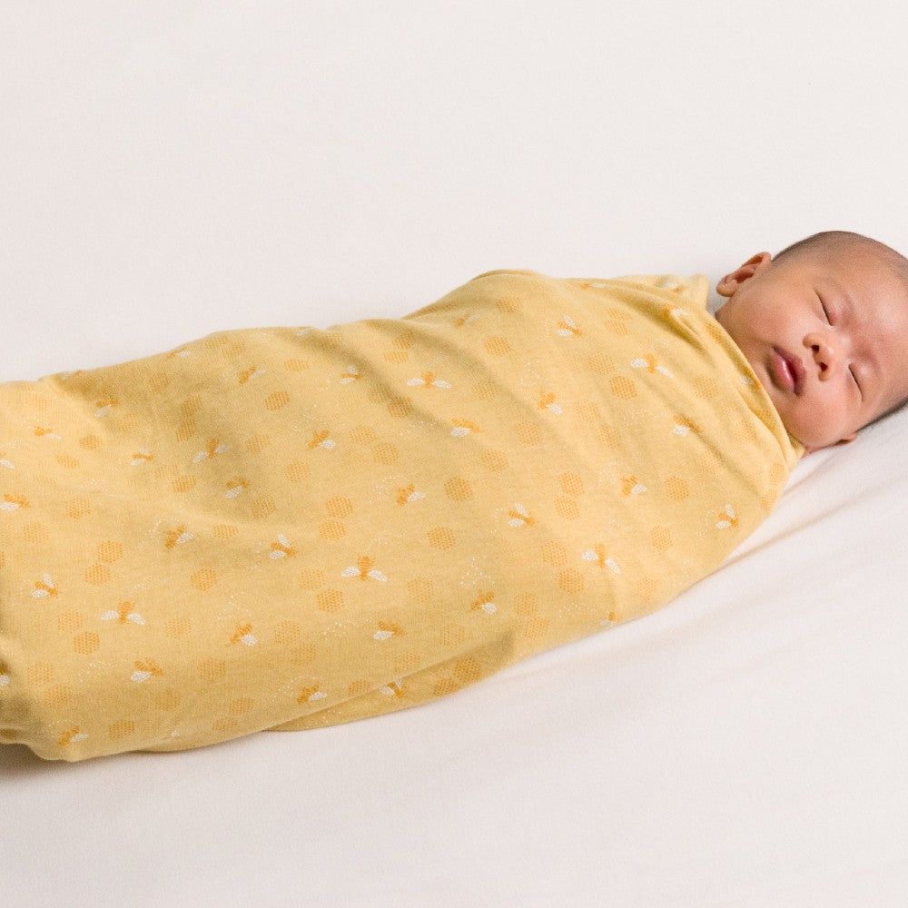 Newborn baby swaddled in a yellow blanket with white patterns on a light gray background