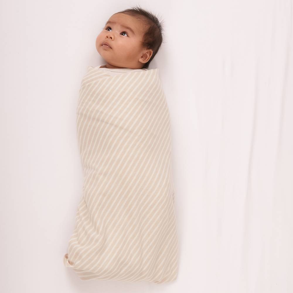 Baby wrapped in a beige swaddle on a white background