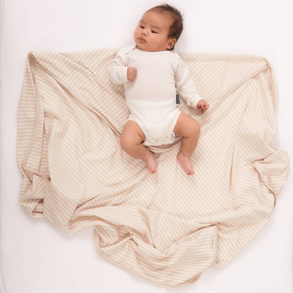 Baby in a white onesie lying on a beige textured blanket