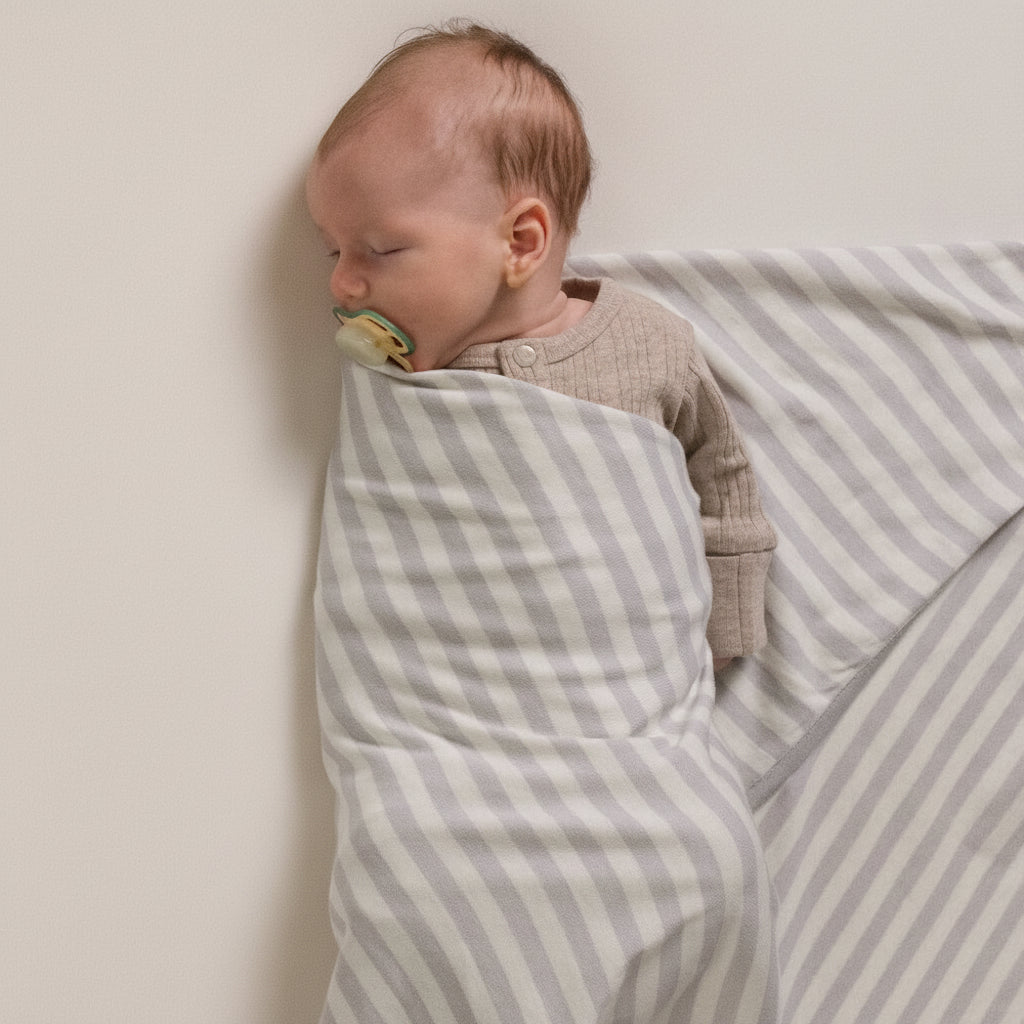 Baby swaddled in a gray and white striped woolbabe swaddling blanket with a pacifier.