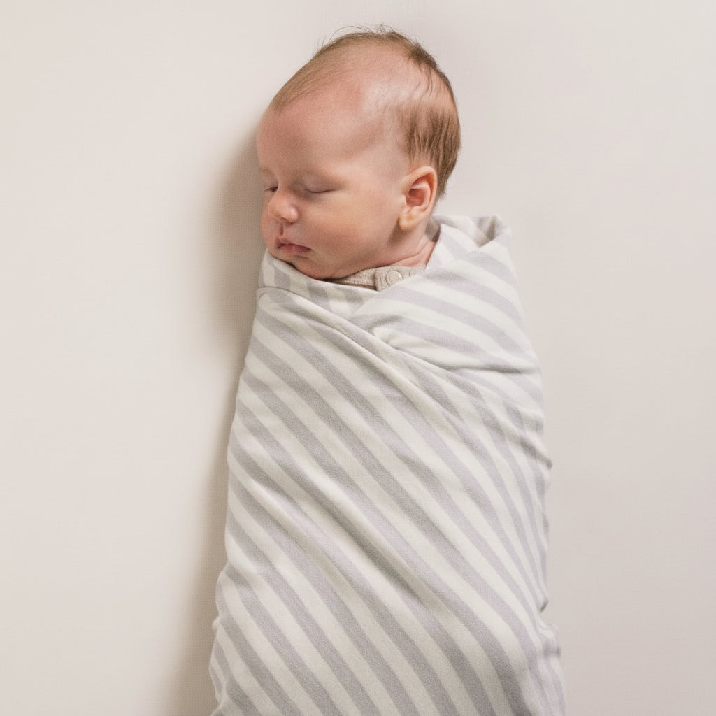 Baby swaddled in a striped blanket , against a plain background