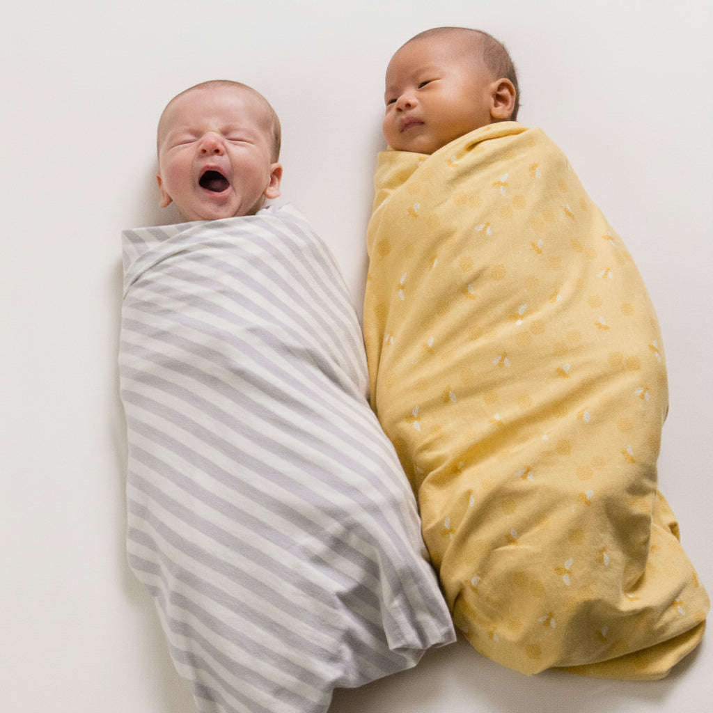 Two babies swaddled in gray striped and yellow blankets on a white background