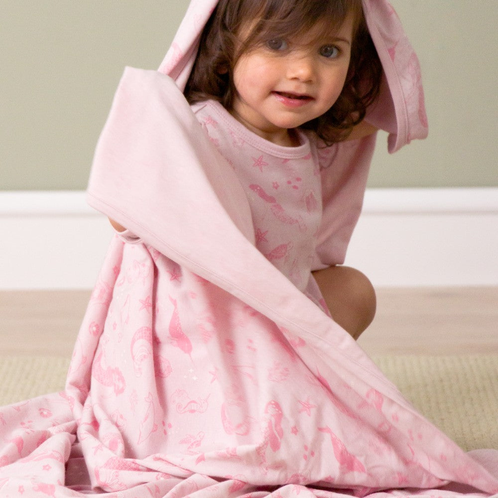 Child wrapped in a pink blanket with butterfly pattern on a light background