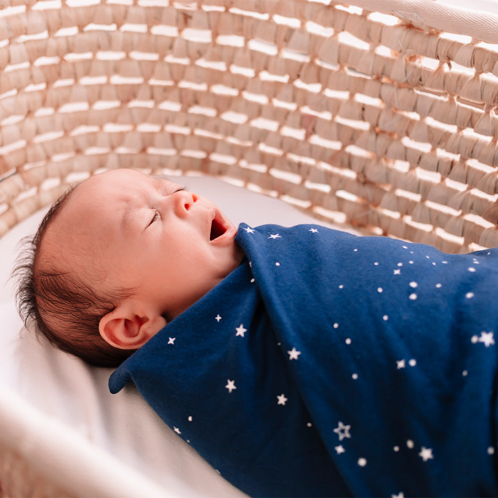 Newborn baby wrapped in a blue blanket with white stars, lying in a woven basket.