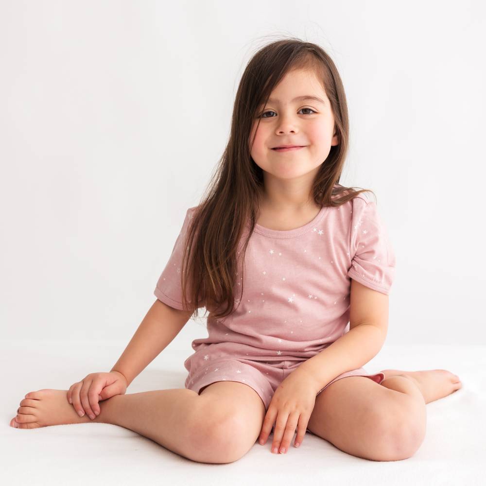 Young girl wearing a pink outfit with white polka dots sitting on a white background