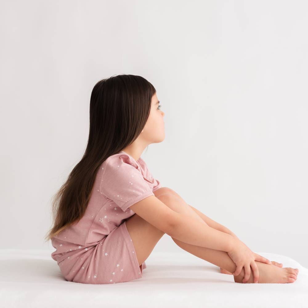 Woman in a pink dress sitting on a white surface with a plain background