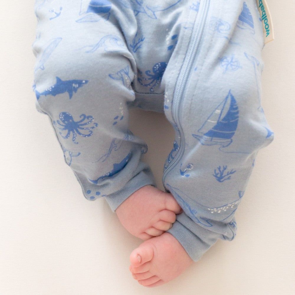 Baby wearing blue pajama pants with sea-themed print on a white background