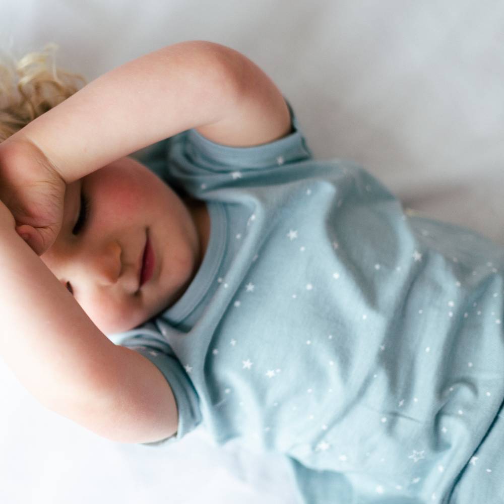 Child wearing a light blue shirt with star patterns, lying on a white surface.