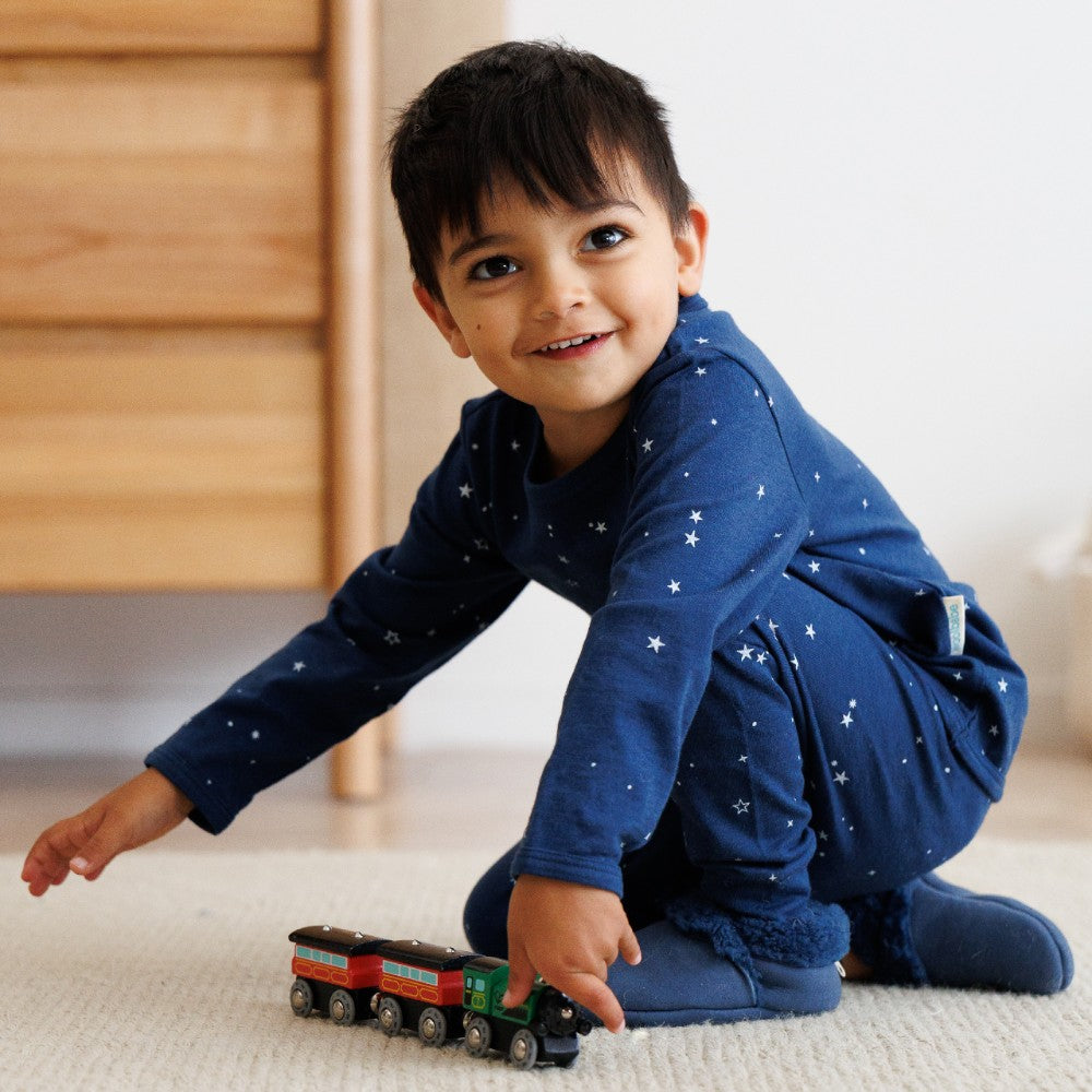 Child playing with a toy train on a carpeted floor wearing tekapo stars navy woolbabe pyjamas 