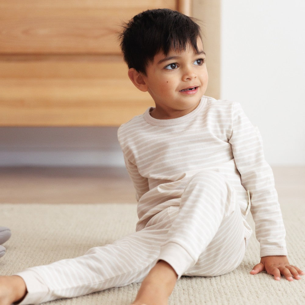 Child wearing a beige stripe woolbabe pyjamas sitting on a couch.