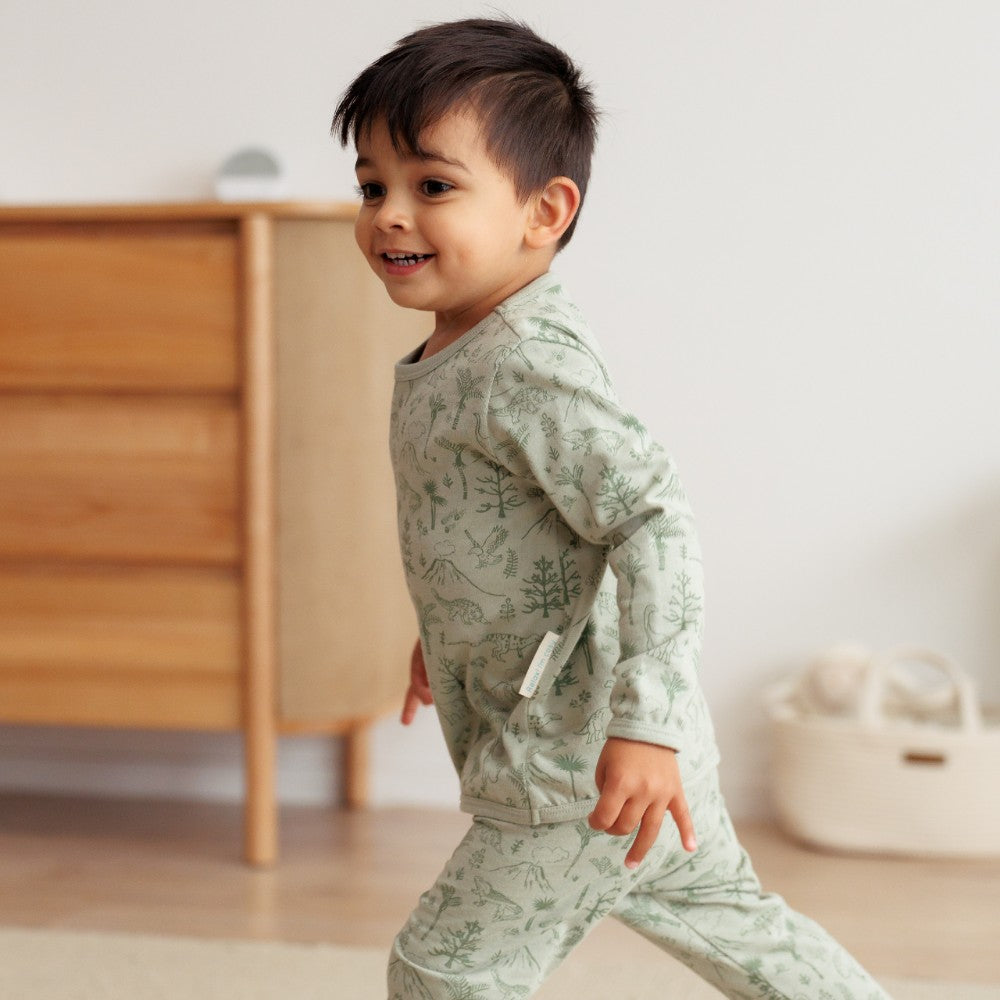 Child wearing a green patterned outfit in a room with wooden furniture.