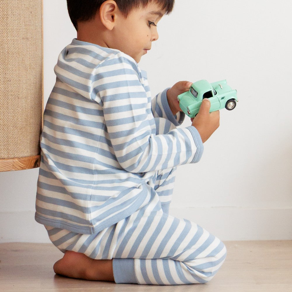 Child in blue and white woolbabe striped pajamas holding a green toy car.
