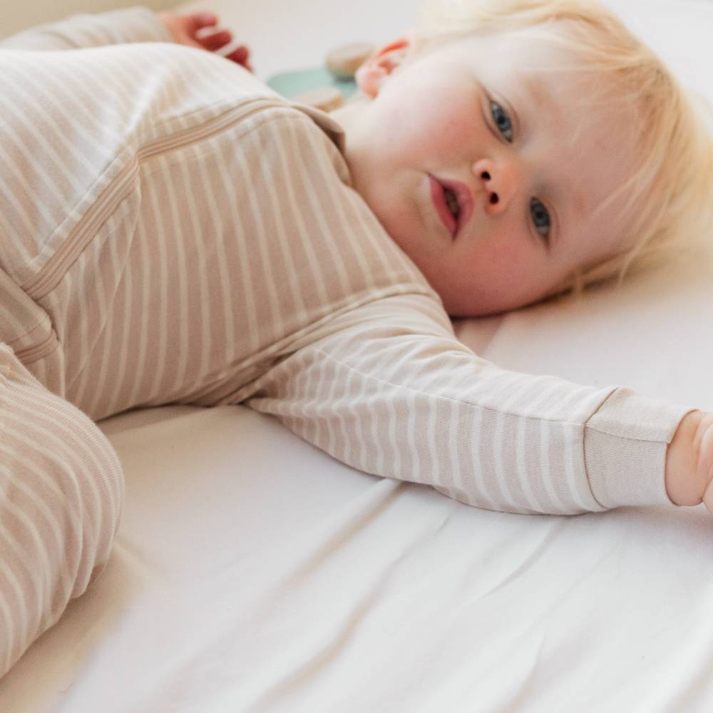 Child wearing a woolbabe striped onesie lying on a white surface