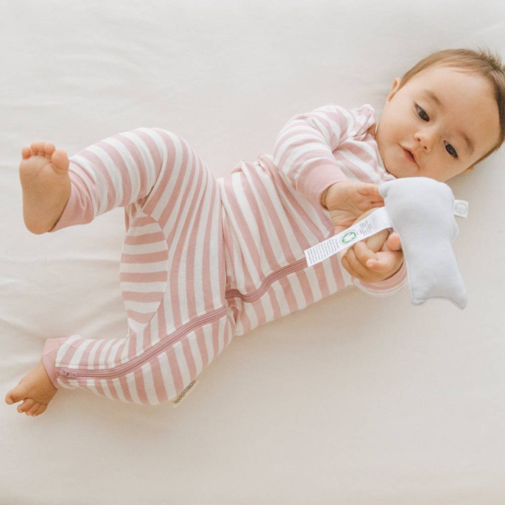 Baby in pink and white striped outfit holding a white toy on a light background
