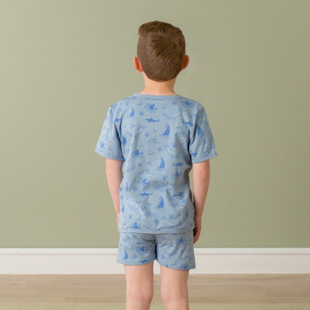 Child wearing a blue pajama set with animal patterns against a plain wall.