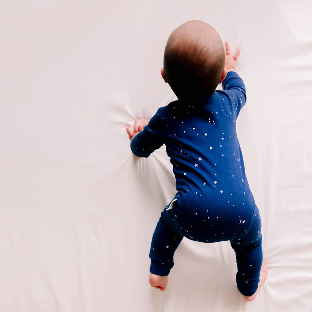 Baby in a blue woolbabe onesie with star pattern crawling on a white surface
