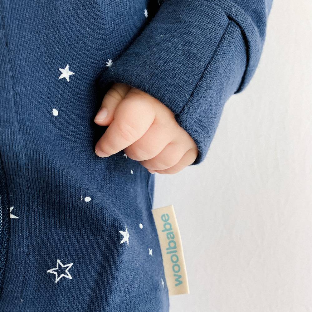 Close-up of a child's hand holding a blue garment with star patterns and a 'woolbabe' tag.