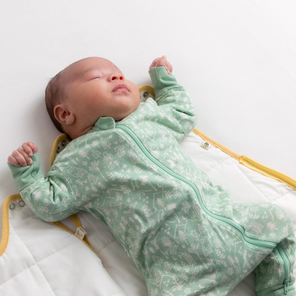 Baby in a green onesie with white patterns lying on a white surface