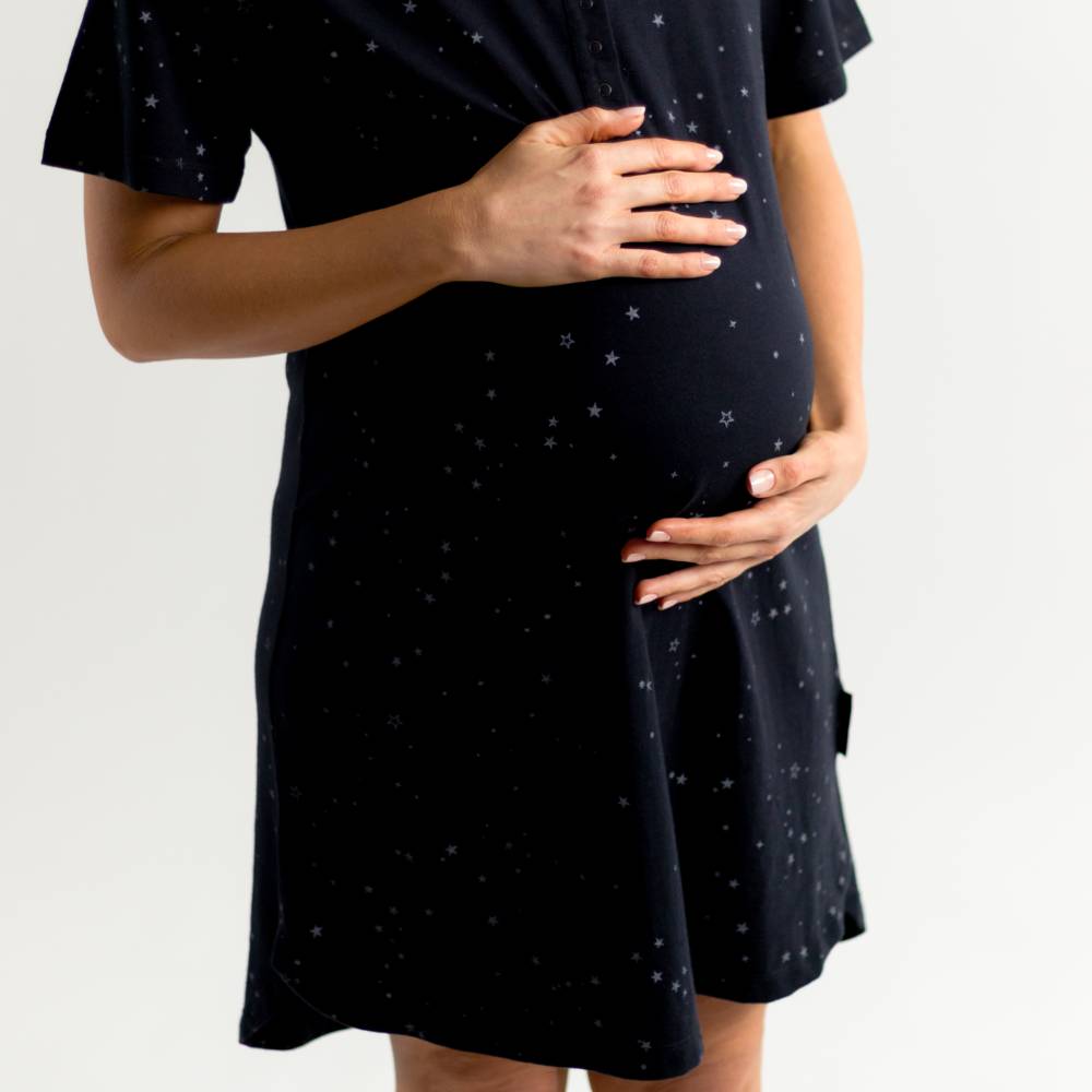 Pregnant person wearing a black dress with star pattern on a white background