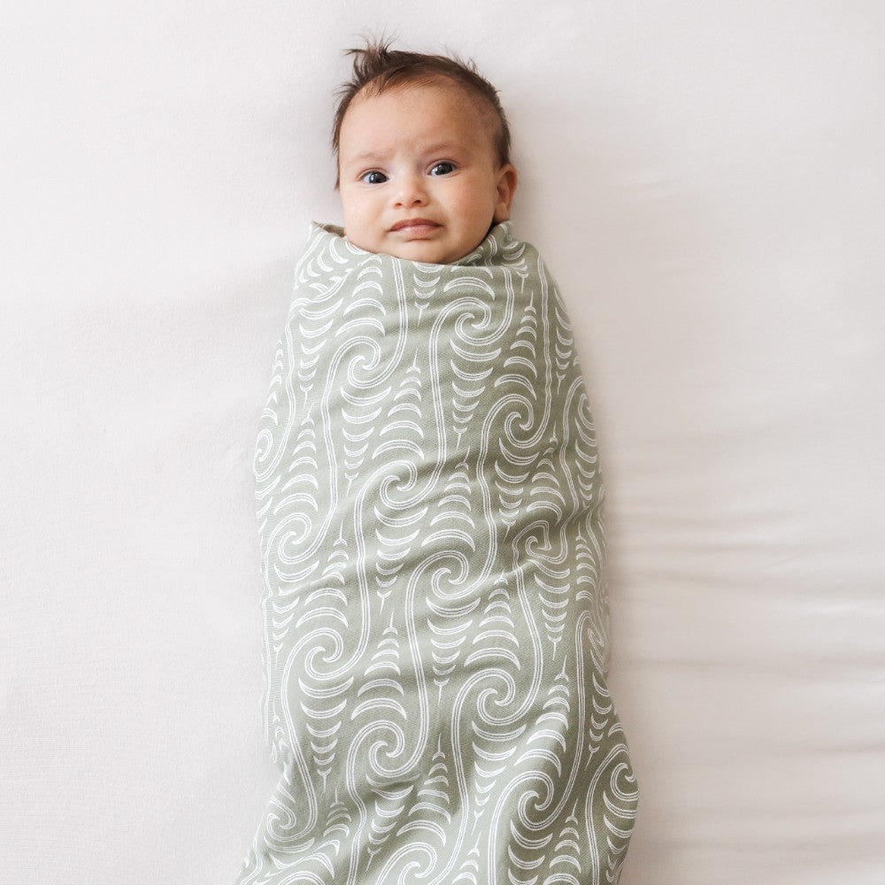 Baby swaddled in a merino wrap with maori patterned blanket on a white background