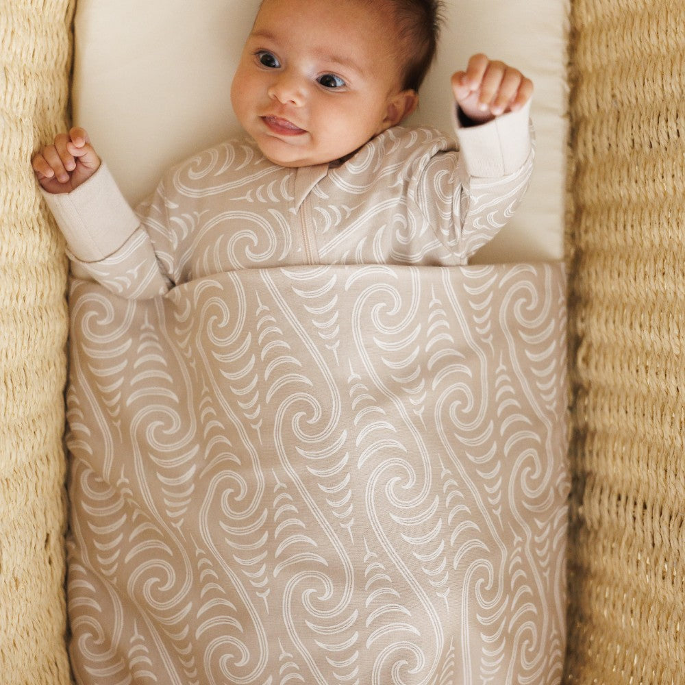 Baby wrapped in a Maori patterned woolbabe swaddle blanket on a textured surface