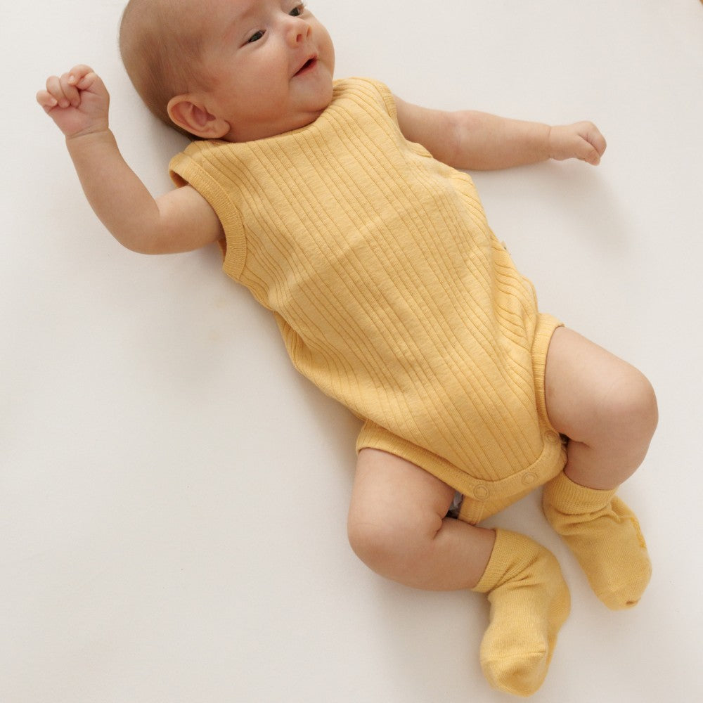 baby wearing yellow merino socks and singletsuit on white background