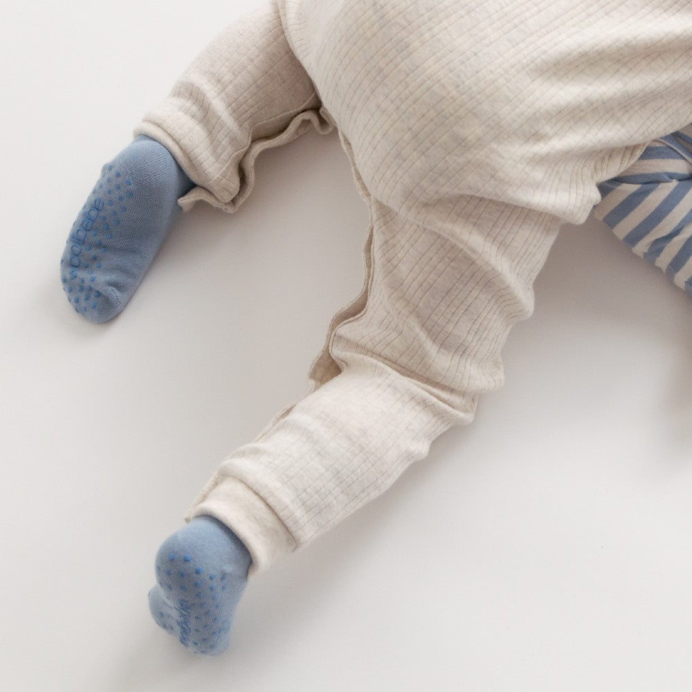 Baby wearing beige onesie and blue grippy socks on a light background