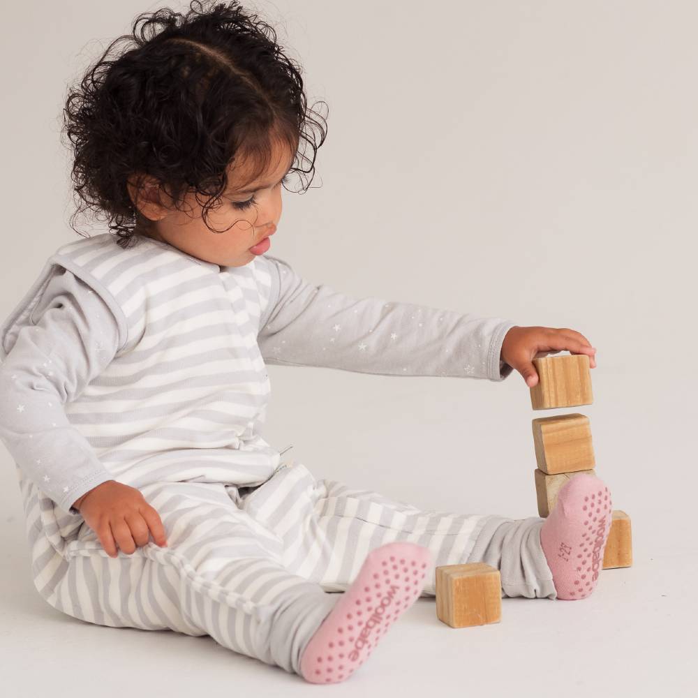Child playing with wooden blocks on a plain background wearing pink grippy socks with woolbabe logo