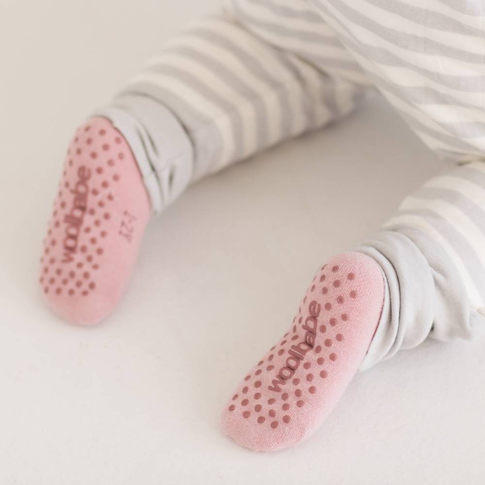 Baby's feet wearing pink socks with textured sole on a light background