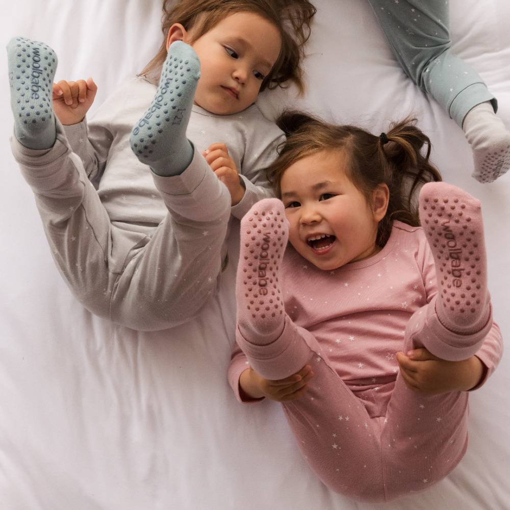 Two children wearing slipper socks with textured soles on a white bed.