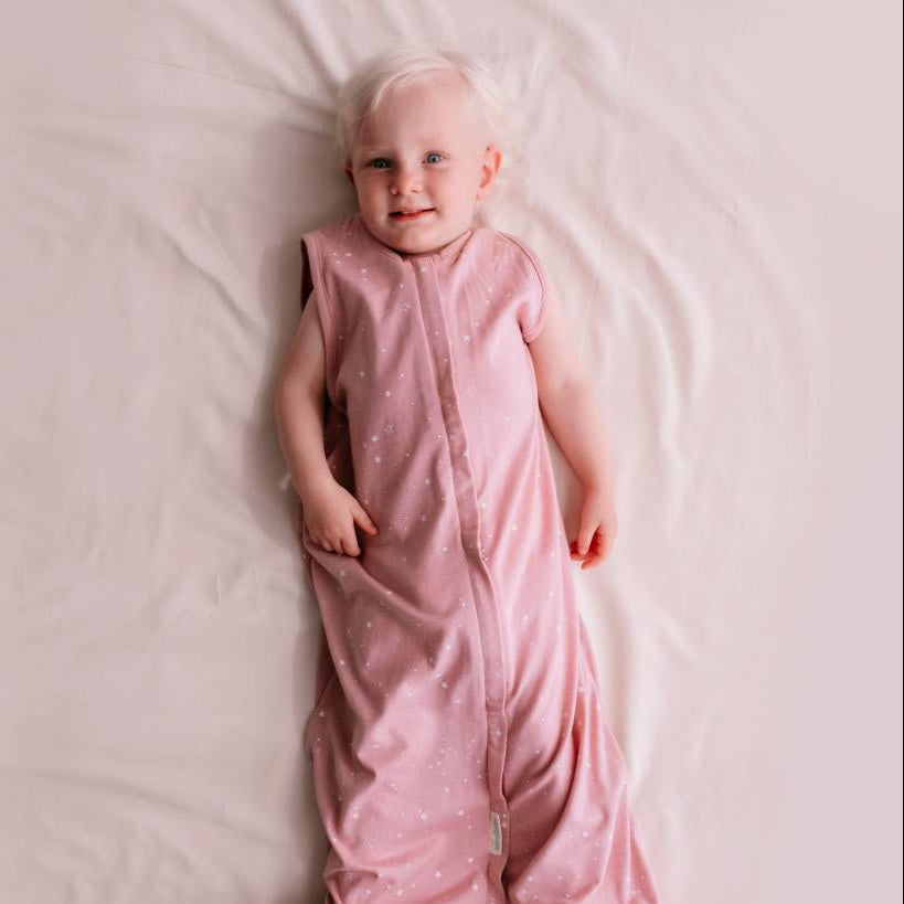 Child wearing a pink sleeping bag on a light pink blanket