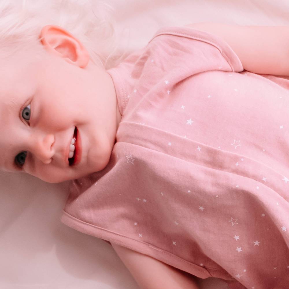 Baby wearing a pink sleep sack with star patterns on a light background