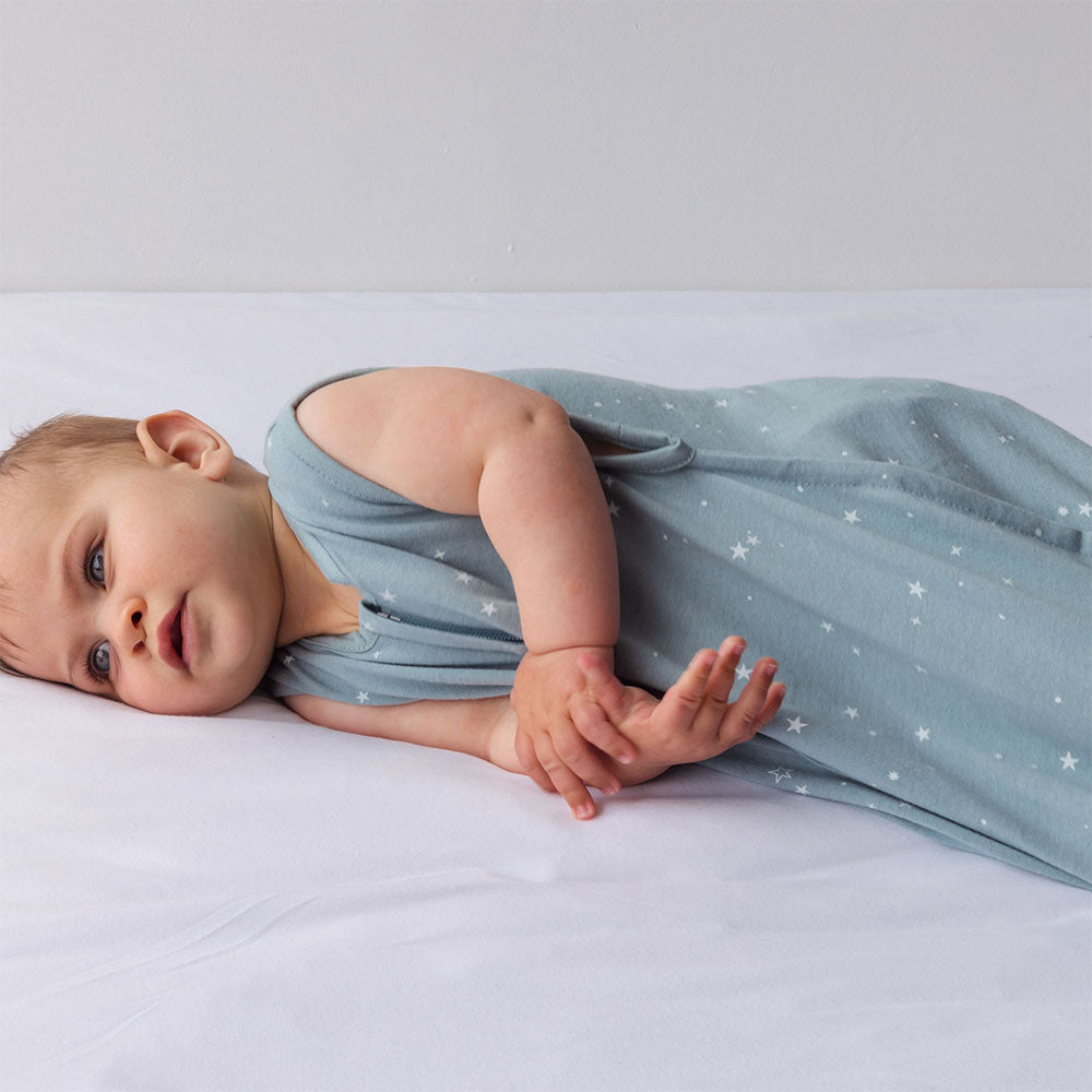 Baby lying on a white surface wearing a light blue summer sleep sack with star pattern.