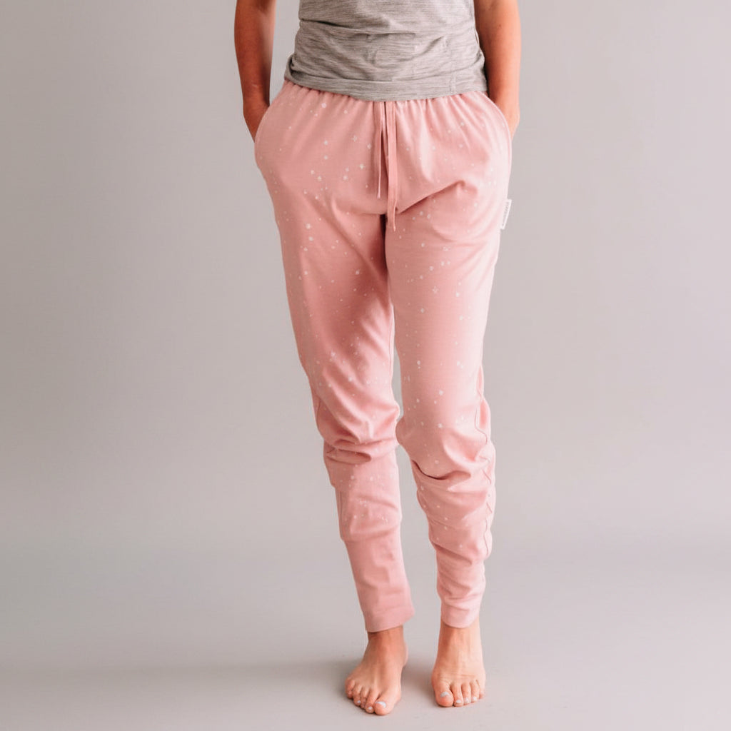 Person wearing pink pajama pants with a subtle pattern in a room with a wooden floor and teal wall.