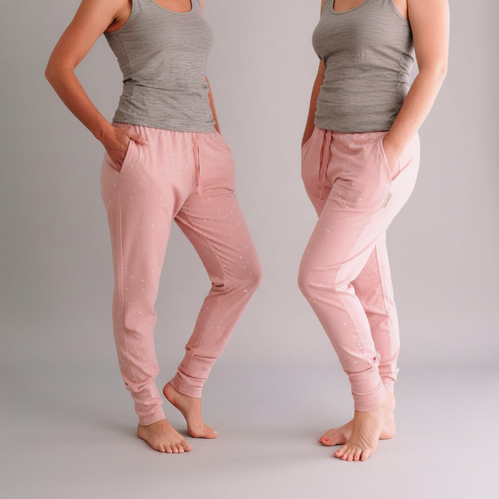 Person wearing pink polka dot pants standing on a wooden floor with a grey wall in the background.