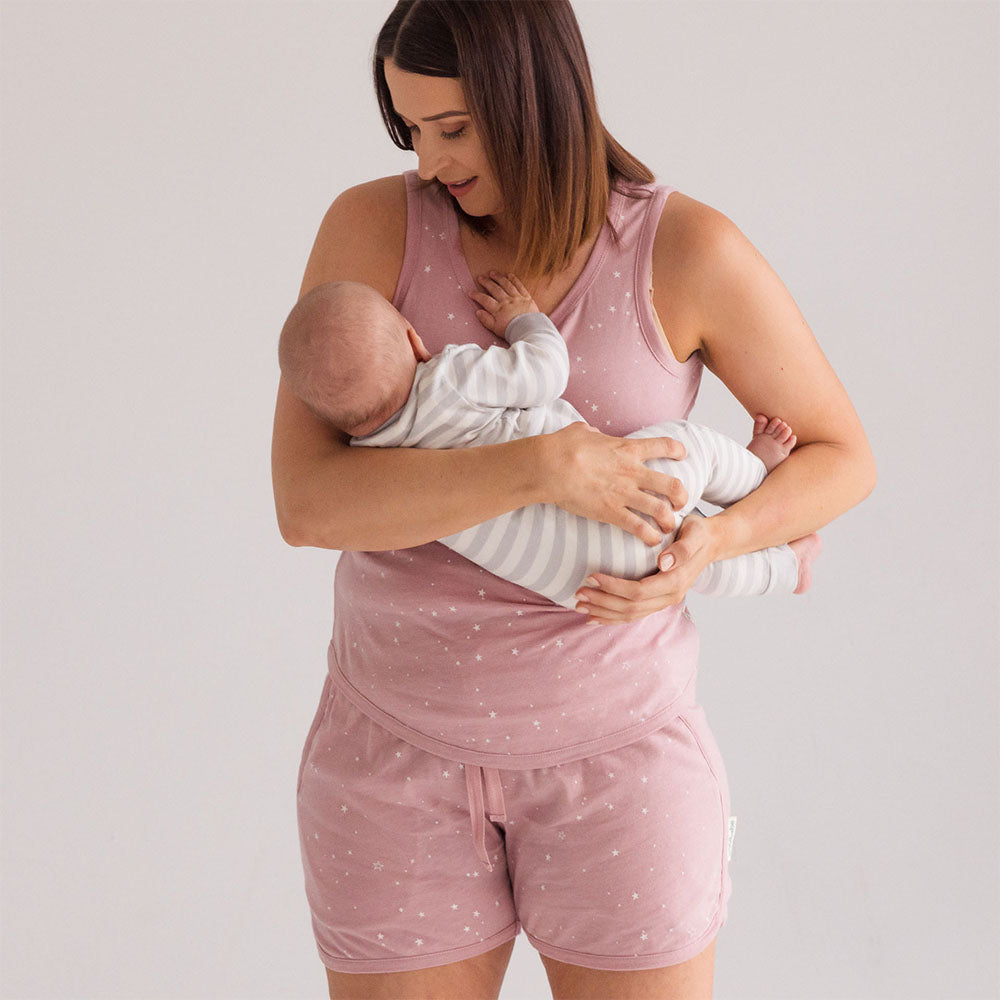 Woman in pink pajama set holding a baby against a plain background