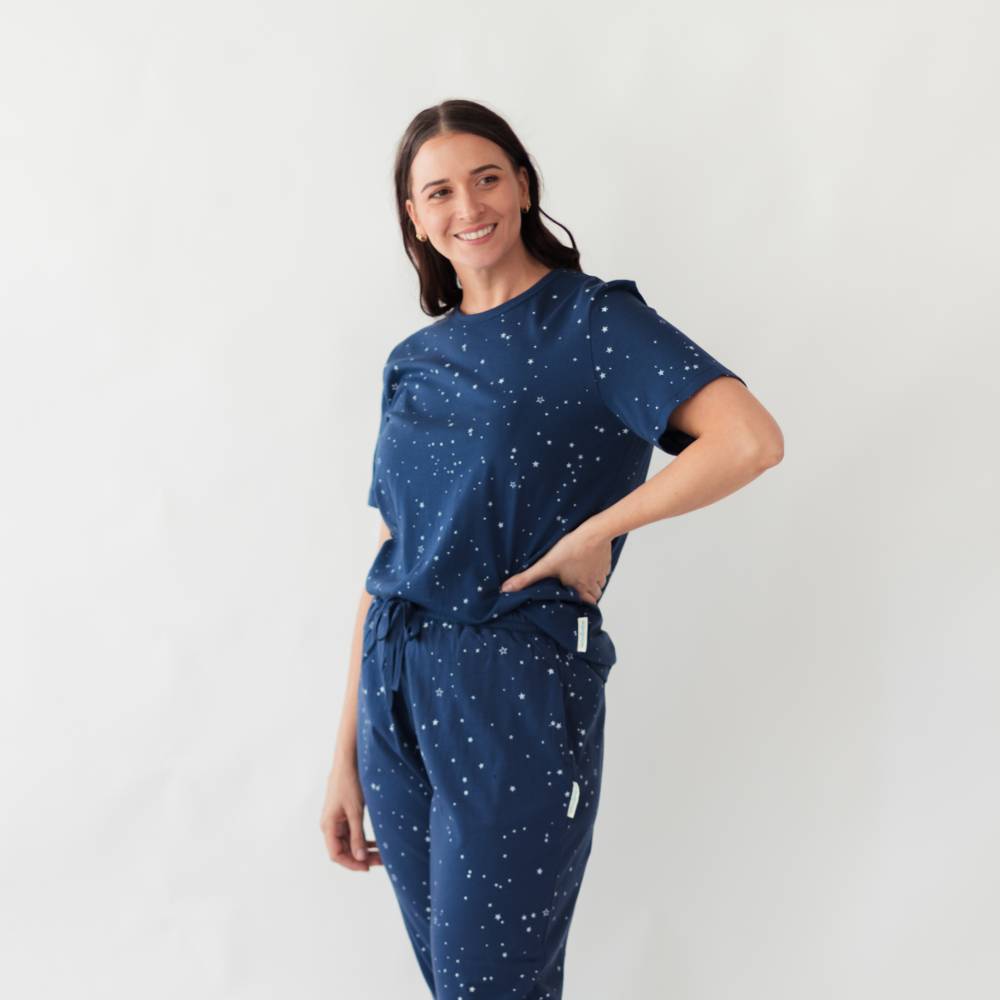 Woman wearing a bluelounge top and lounge pants from woolbabe with star patterns on a white background