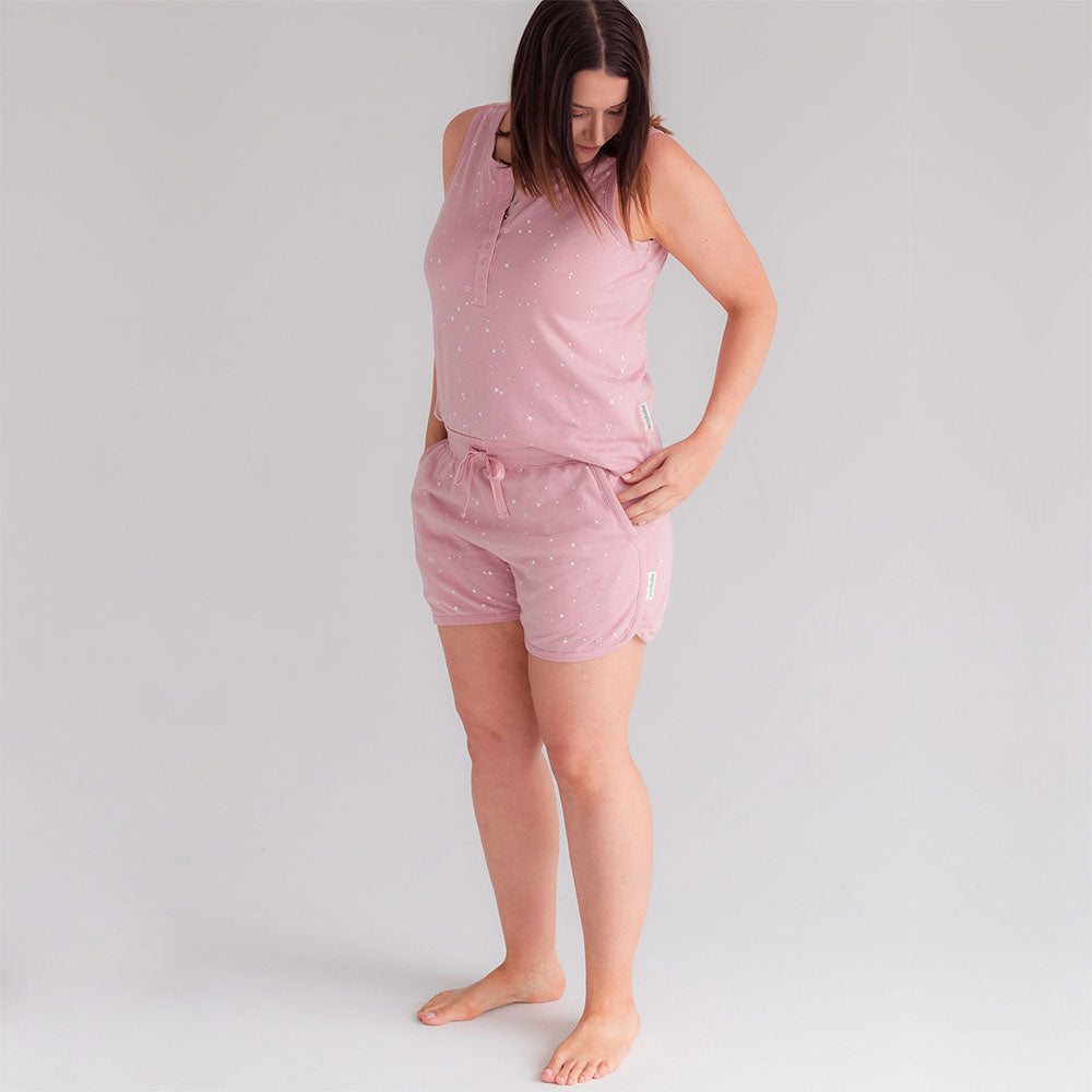 Woman wearing a pink woolbabe pajama set with white stars on a light gray background